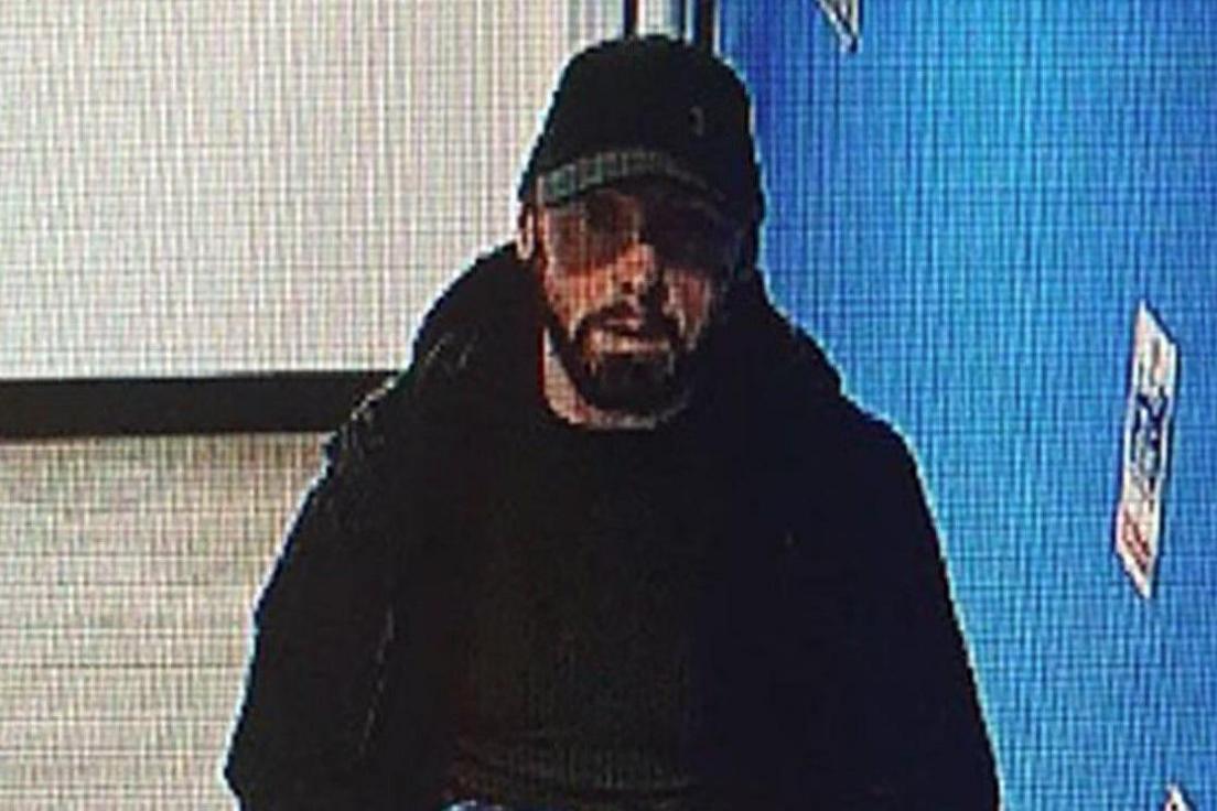 A CCTV image of James Clacher. He wears dark clothing and carries a bag while walking along a hallway