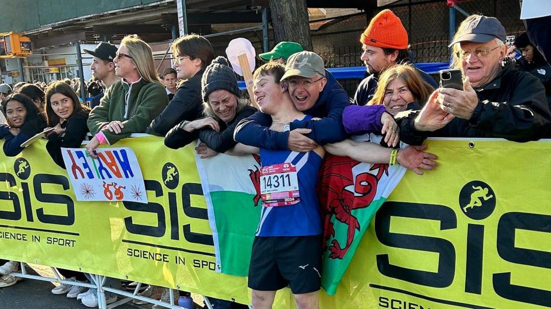 Lloyd being embraced by family at the finish line, with a Welsh flag around his shoulders