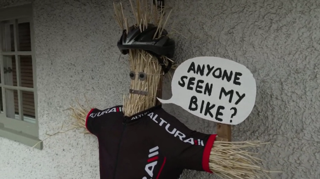 Straw has been put into the sleeves and neck hole of a cyclist's black top to make outstretched arms and a long head. On top is a grey bike helmet and a white speech bubble which reads 'anyone seen my bike?' The straw face has been given eyes and a mouth.