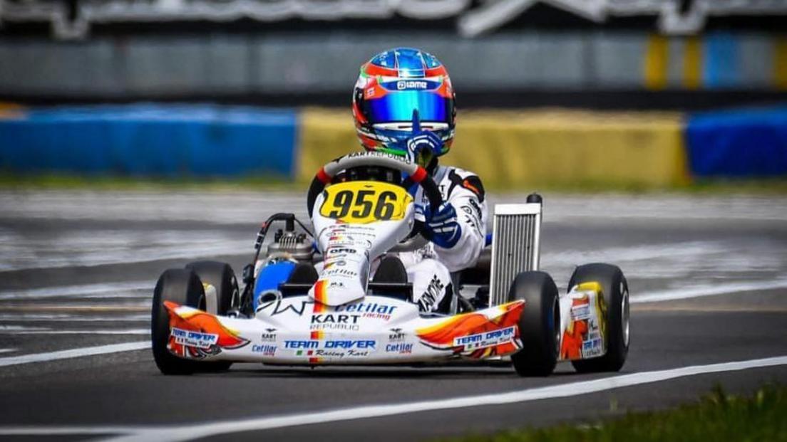 A go-kart covered in logos and branding with a driver wearing a reflective blue helmet