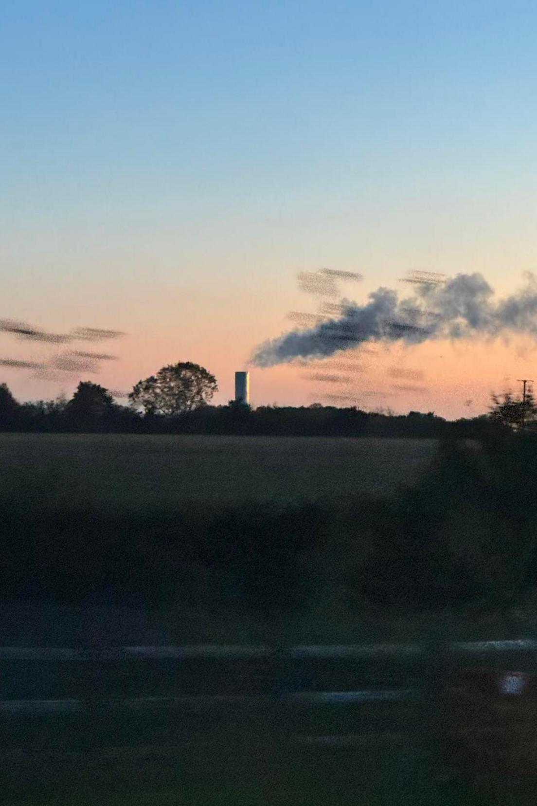 The sun appears to be setting and there is a plume of steam coming from a chimney on the horizon.