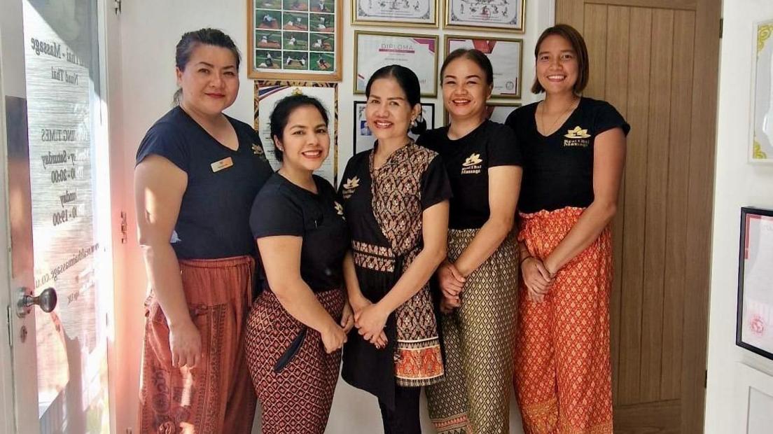 Maneerat Bossog standing in the middle of a group of women. She has two women on either side of her. They are all smiling at the camera and wearing black tops and colourful trousers