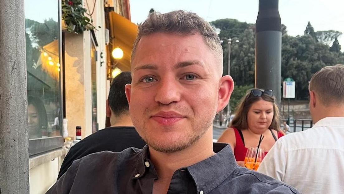 Head and shoulders image of Philip Robinson, a young man, sitting outside a restaurant wearing a dark shirt