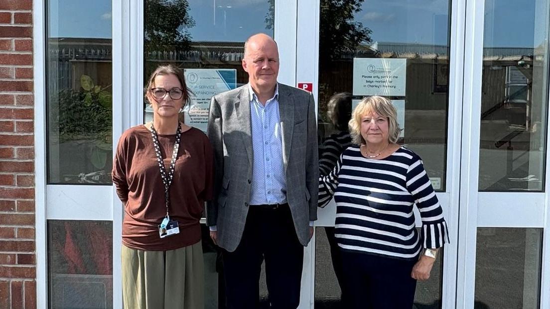 Ashley Fox is standing between Dawn Carey and Doreen Smith in front of the building housing the charity. Mr Fox is wearing a suit jacket over a blue shirt.