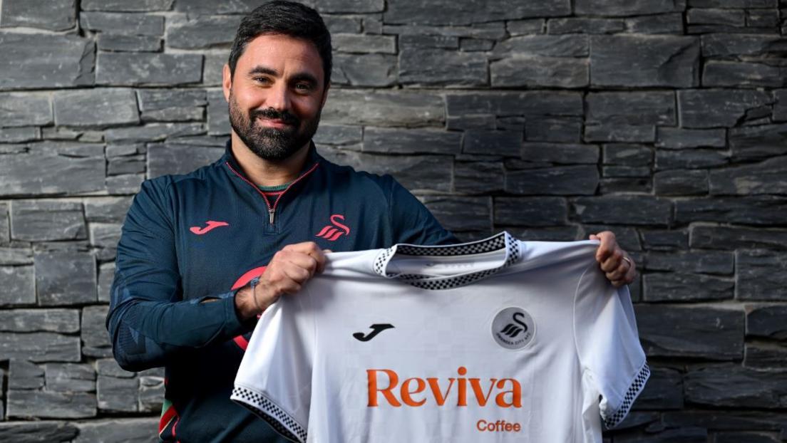 Vitor Matos has dark hair and dark beard and is holding a white Swansea City football shirt