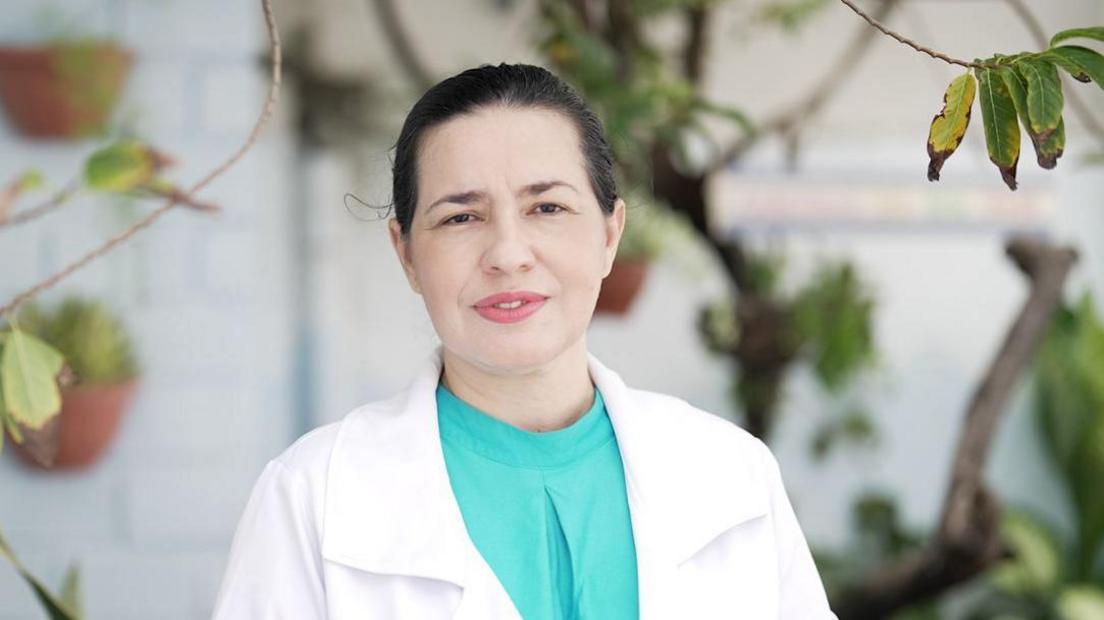 Mardjane Lemos looks at the camera while wearing a turquoise blouse underneath a white doctor's coat.