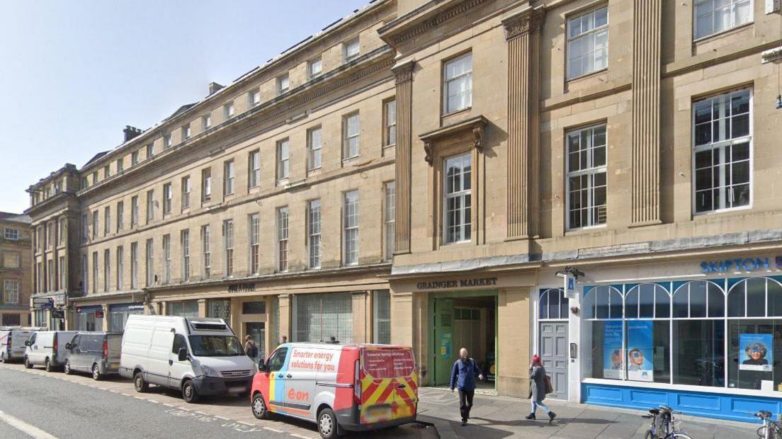 Exterior of Grainger Market, which is a four-storey Georgian sand-coloured stone building lined with tall white windows.