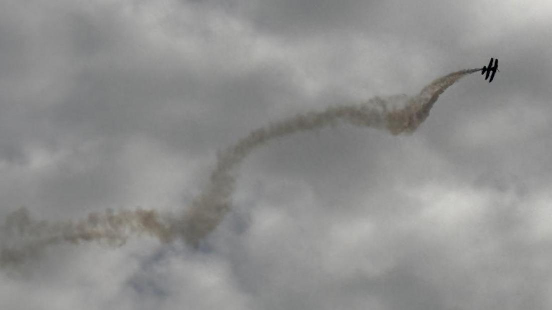 A large plume of grey smoke spiralling out the back of two small planes, which are in flight.