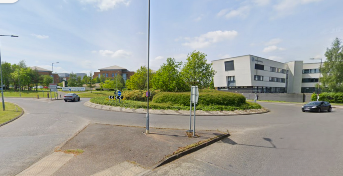 Two cars travelling around the roundabout on Colney Lane with the Norfolk and Norwich University Hospital in the background