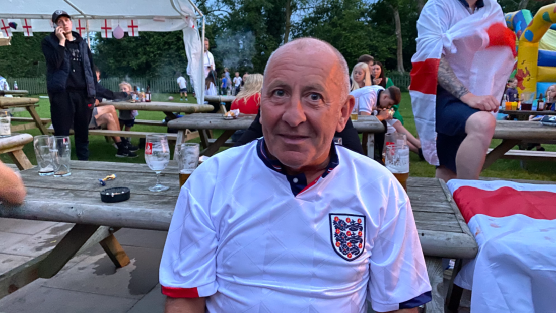 Gary Leonard, wearing a white England top. He is sitting on a bench in a pub garden