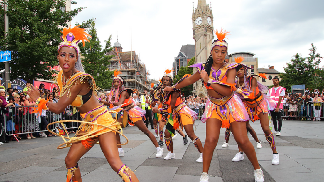 Women dressed in colourful costumes dancing in the Leicester Caribbean Carnival troops in the parade near the clocktower in the city centre