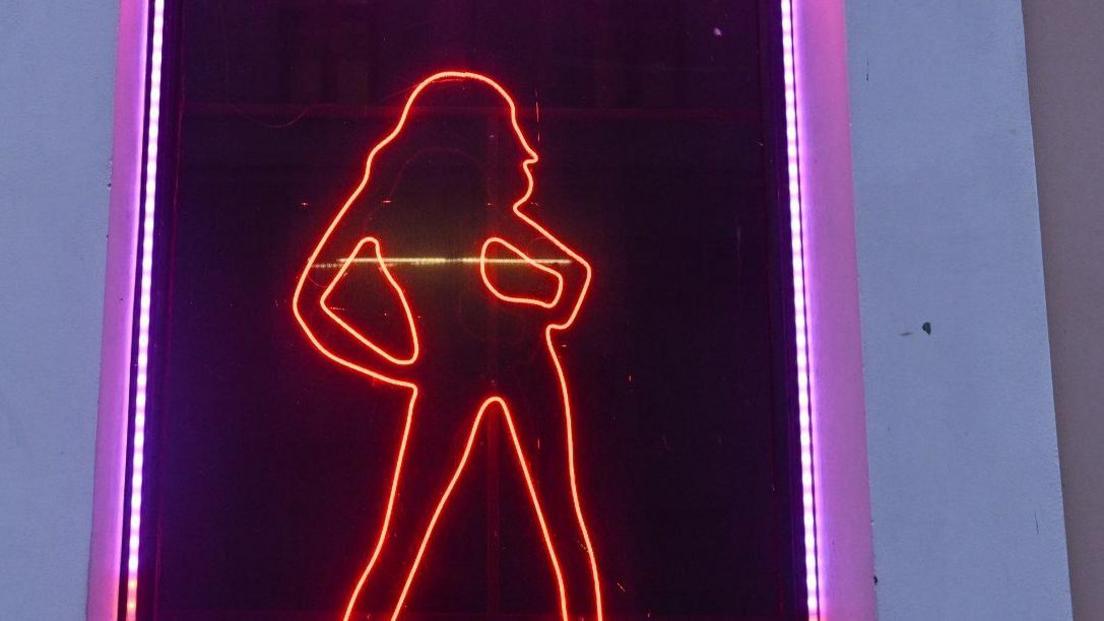 A red neon light in the silhouette of a woman with her hands on her hips