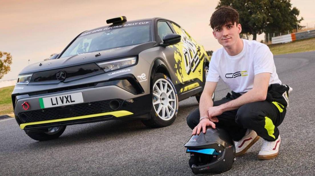 Llun yn dangos dyn ifanc wedi plygu lawr wrth ymyl car llwyd a melyn