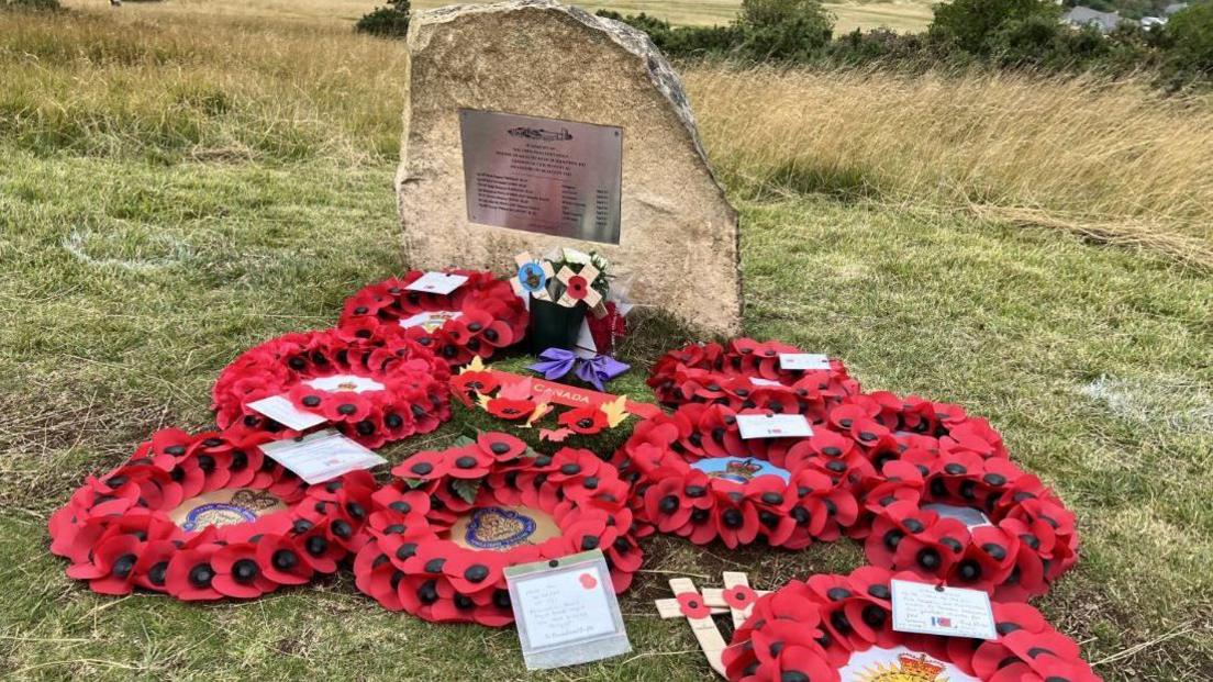 A group of poppy wreaths in front of a stone memorial to the crash victims 