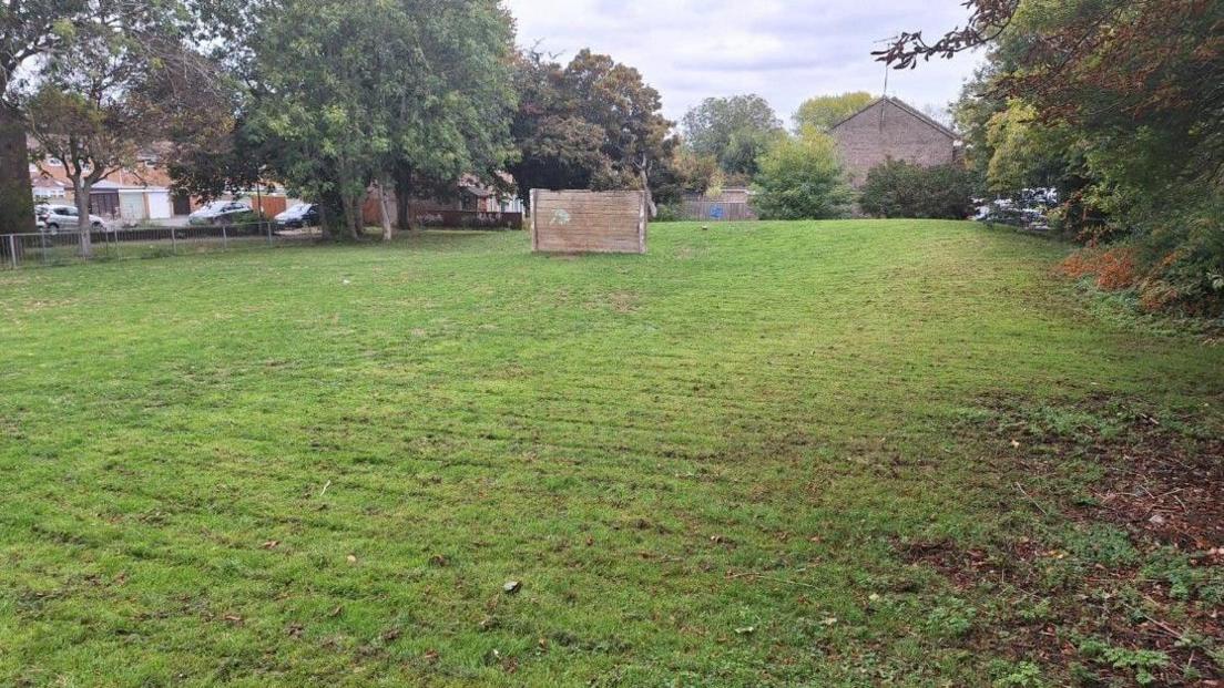 A patch of green space off White Edge More in Liden. There is a wooden screen in the middle of the grass which appears to be used as a goal post for football games.