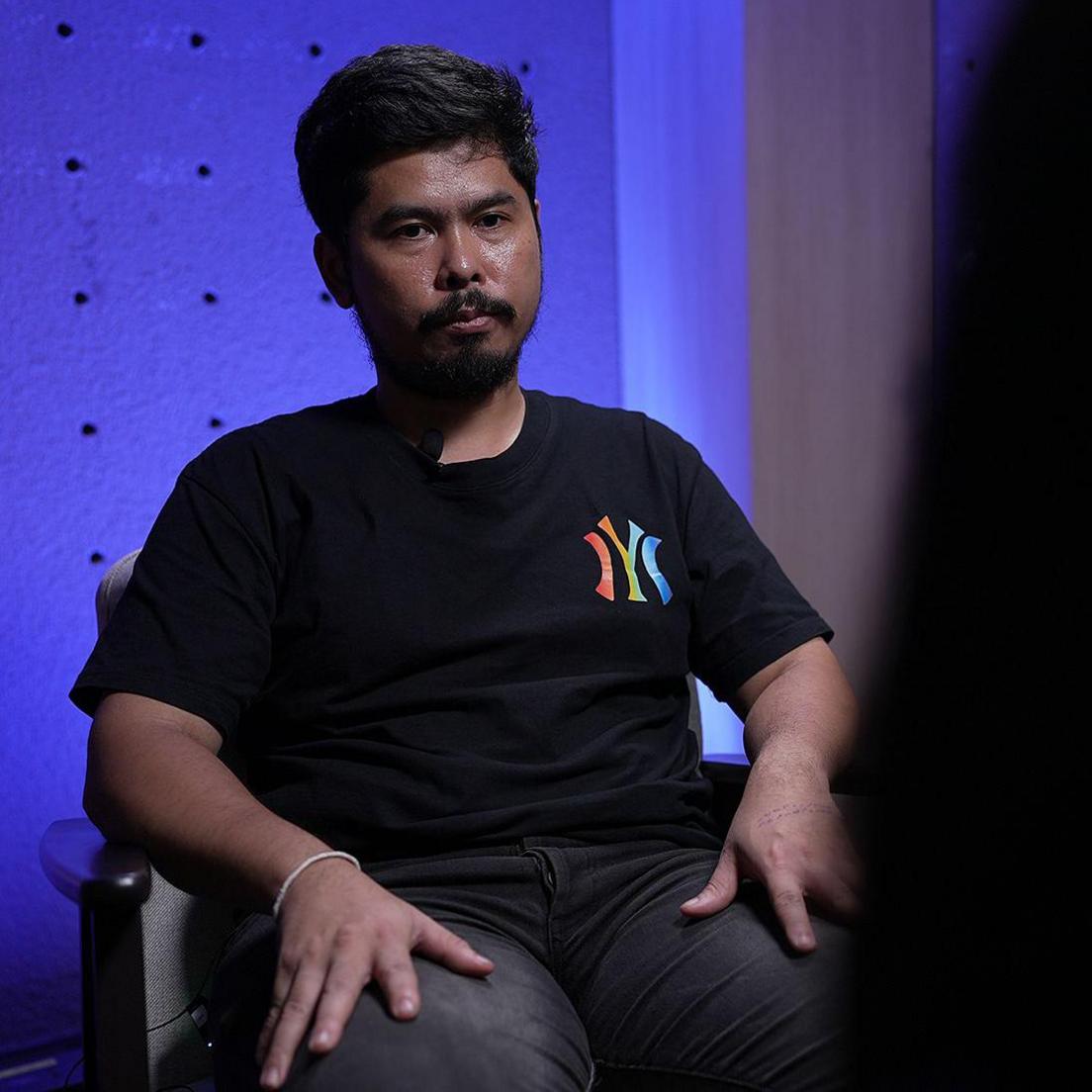 Guitarist Chanate Trasing, in a black T-shirt and black pants, sits during an interview with BBC Thai