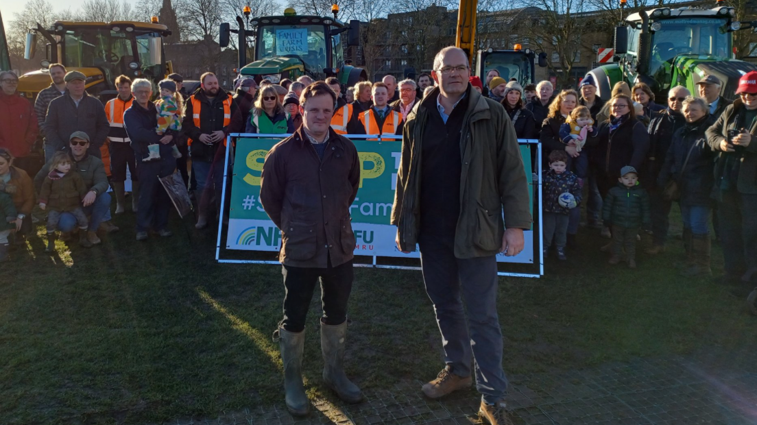 group of banner-holding protesters listening to a man in a green jacket