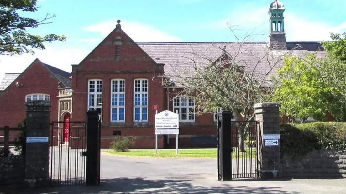 Ysgol Uwchradd Aberteifi, a red bricked building with long white windows and dark gateposts