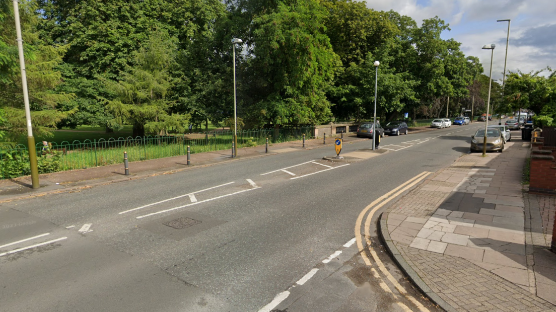 An urban road next to a park with trees in it 