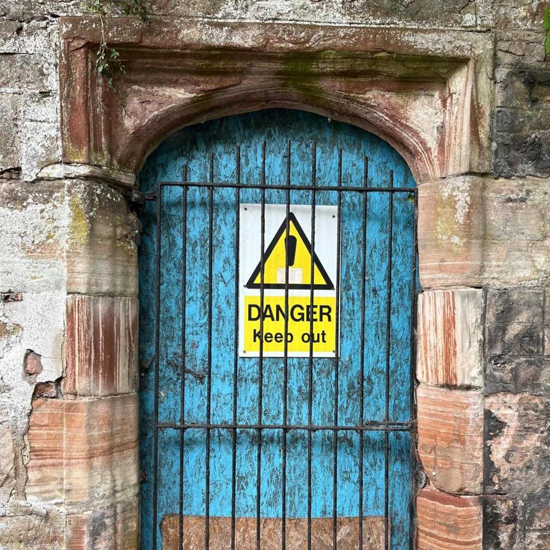 An entrance to Viewhill House blocked by a gate and wooden boards, with a warning sign nailed to a board