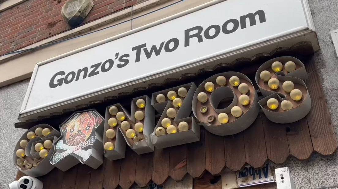 The club's entrance. Above the door, the venue's name features twice, in different styles. At the top, a white sign with black writing says Gonzo's Two Room. Underneath that the club's name appears again, this time with lightbulbs spelling out the word Gonzos.