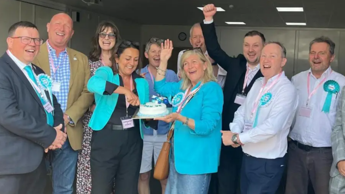 The new group of Reform UK councillors pictured after their emphatic win at the May local elections. A group of 10 people are in the picture, with two councillors in the middle cutting a cake.