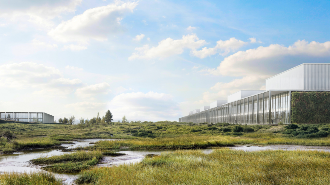 Modern, low-profile buildings with glass facades sit on the right side of a wide, open landscape of marshy grass and shallow winding water channels under a bright blue sky with scattered clouds; a smaller similar building appears in the distance on the left.