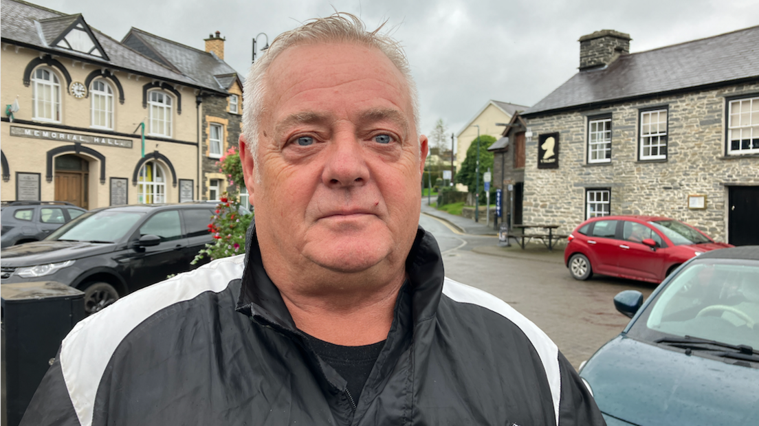 Dilwyn Daniel, wearing a black jacket, standing in front of a high street 