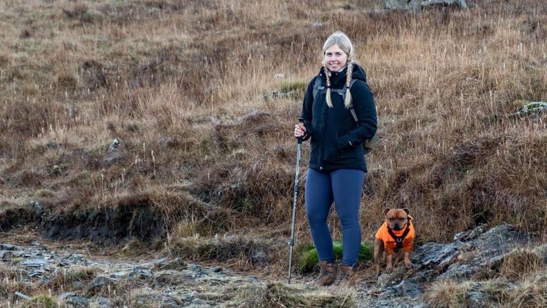 Jennie hiking up a hill, with a little dog by her side.
