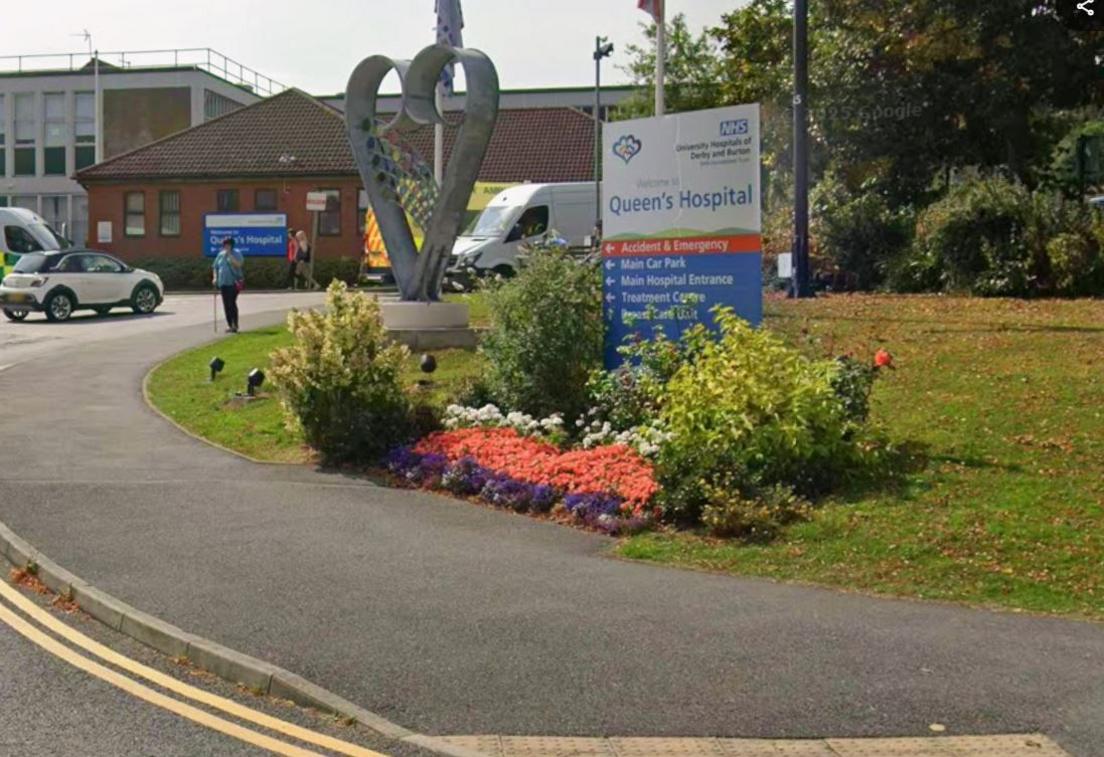 A sign which says "Queen's Hospital" with trees behind
