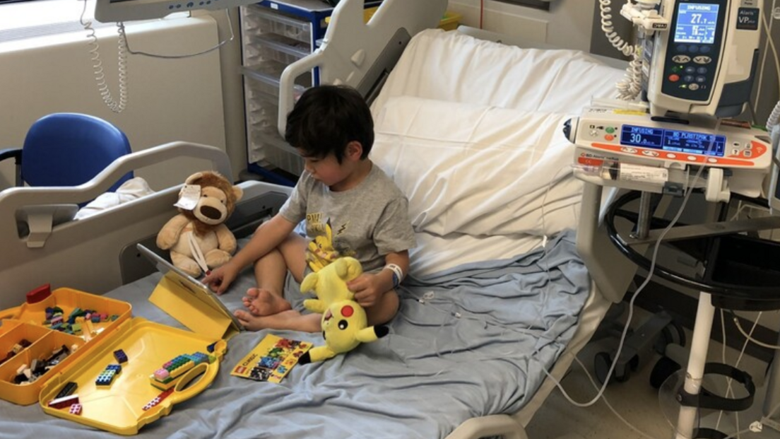 Joshua sitting on a hospital bed with teddy bears, toys and an iPad.