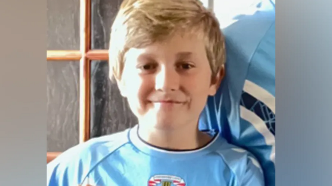 A boy in a blue football top smiles at the camera