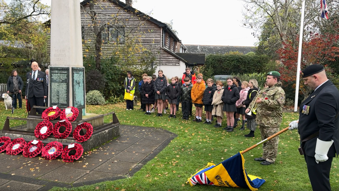 A line of school children beside a war memorial and a flag being lowered during the two minutes' silence