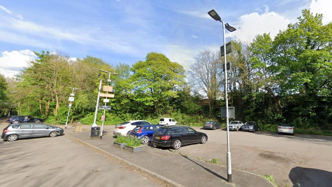 Car park in Wetherby showing about 10 parked cars, with trees and floodlights 