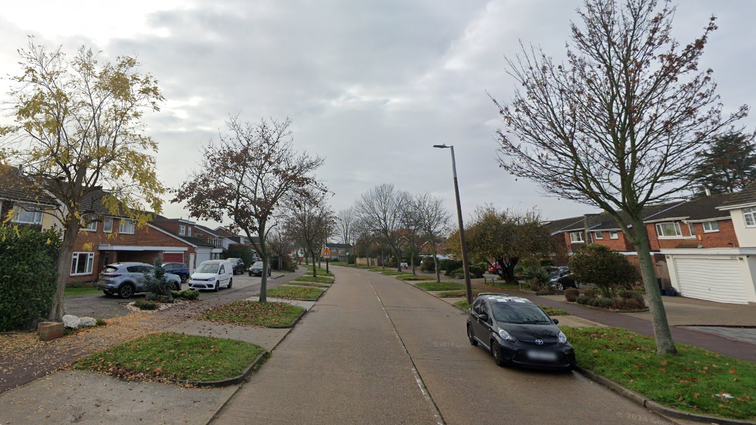 A Google Streetview look at Maplin Way North. A road runs down the middle. Green banks and trees line each side. Then there is a public footpath before the houses which all have large driveways.