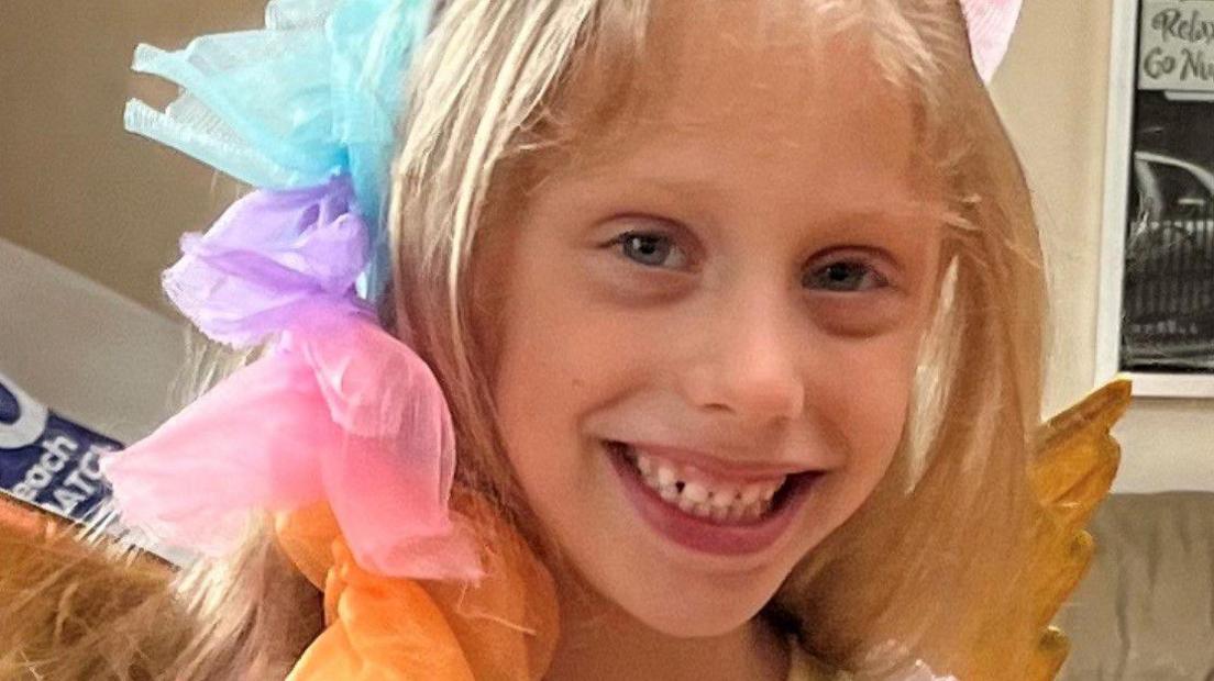 Amelia was smiling at the camera, with her blonde hair around her face. She wore a colourful fancy dress-style outfit with gold wings.
