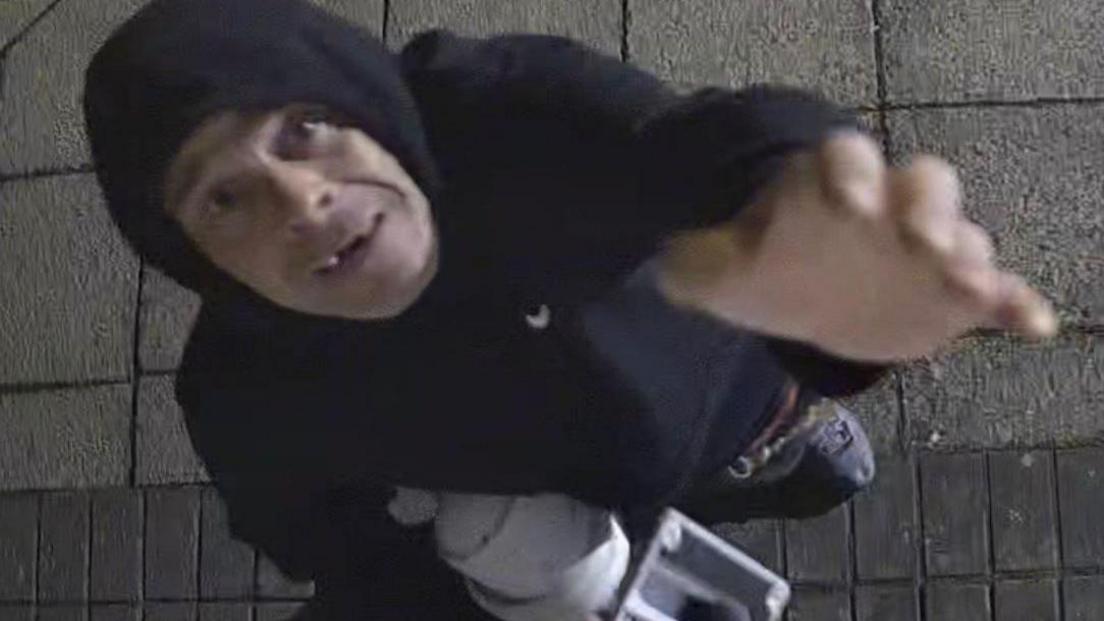 A man with some teeth missing reaching up towards a camera with pieces of white plastic in his other hand