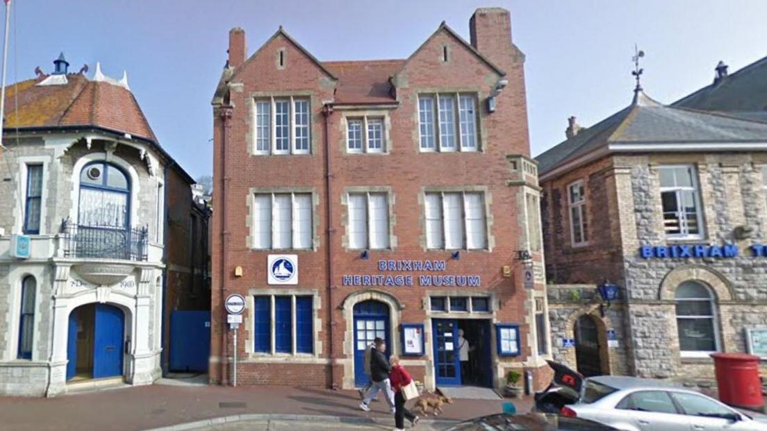 A picture of the outside of the museum. It is a brick building with the name of the museum in blue on the front of it.