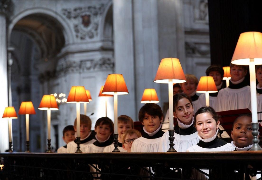 choristers smiling next to lamps in catherdral. 