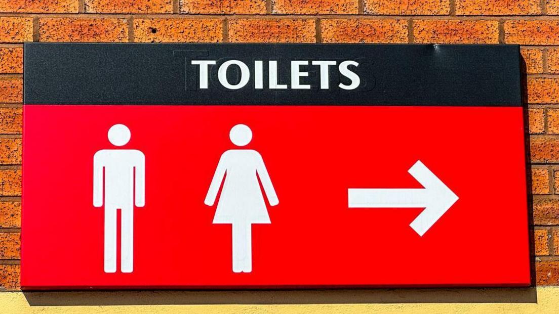 A large red sign with white lettering which reads Toilets, with a picture of a man and a woman below it