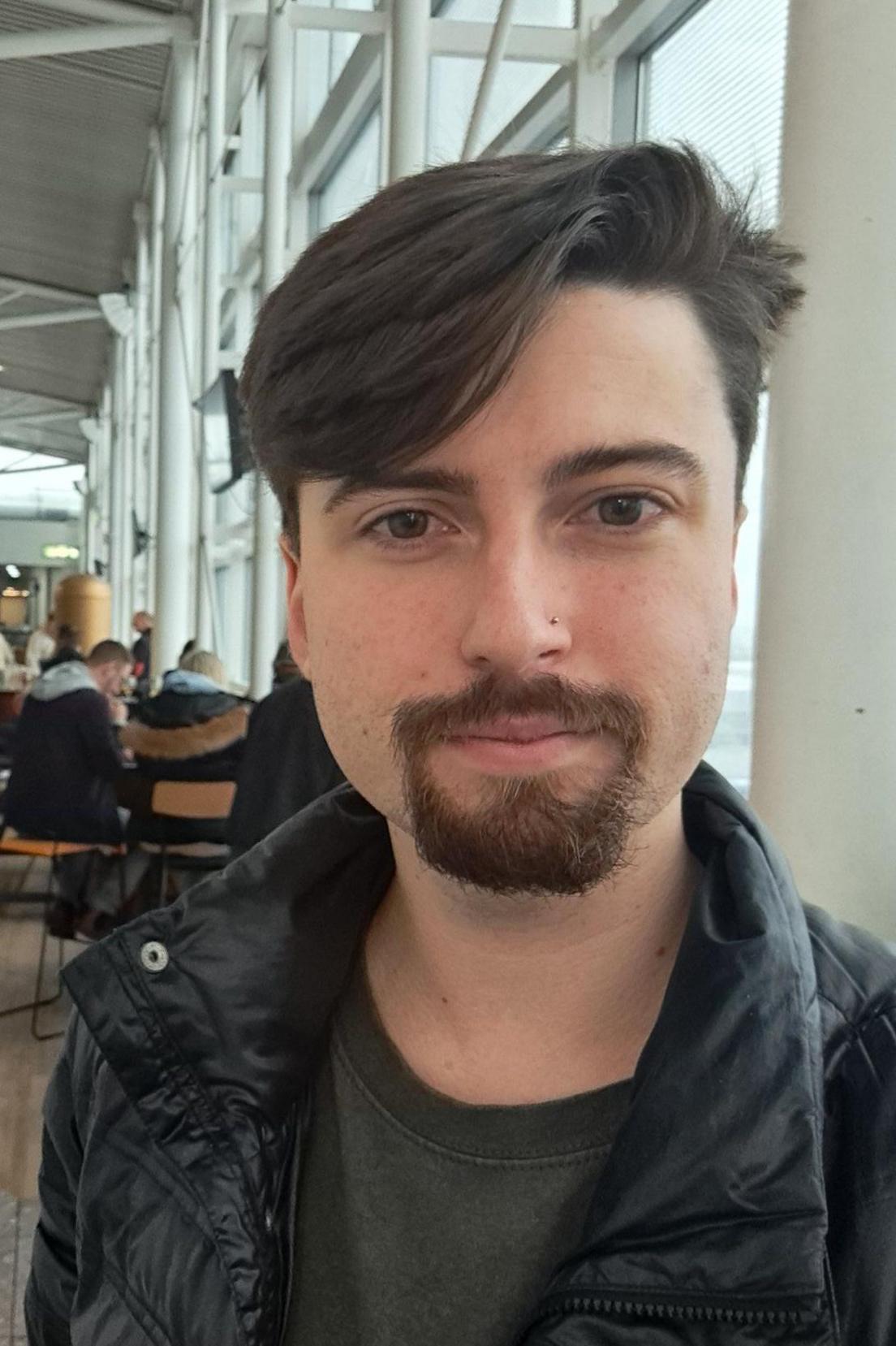 Richard Green at Newcastle Airport. He has dark hair brushed to one side and a goatee beard. He is wearing a black jacket and a dark top.