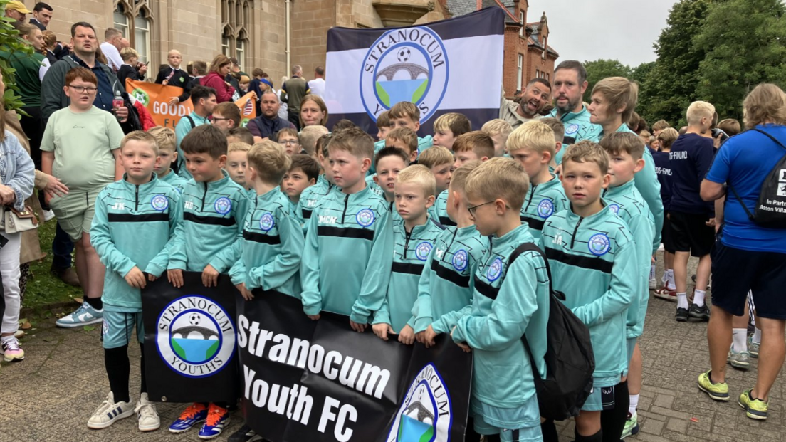Shows boys in green football strips and carrying a banner of Stranocum Youth FC