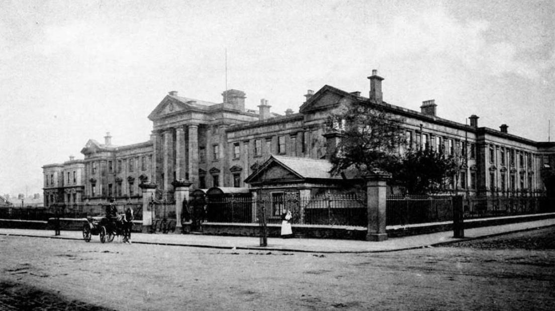 A blurry black and white image of the old hospital building with a horse and carriage on the road outside.