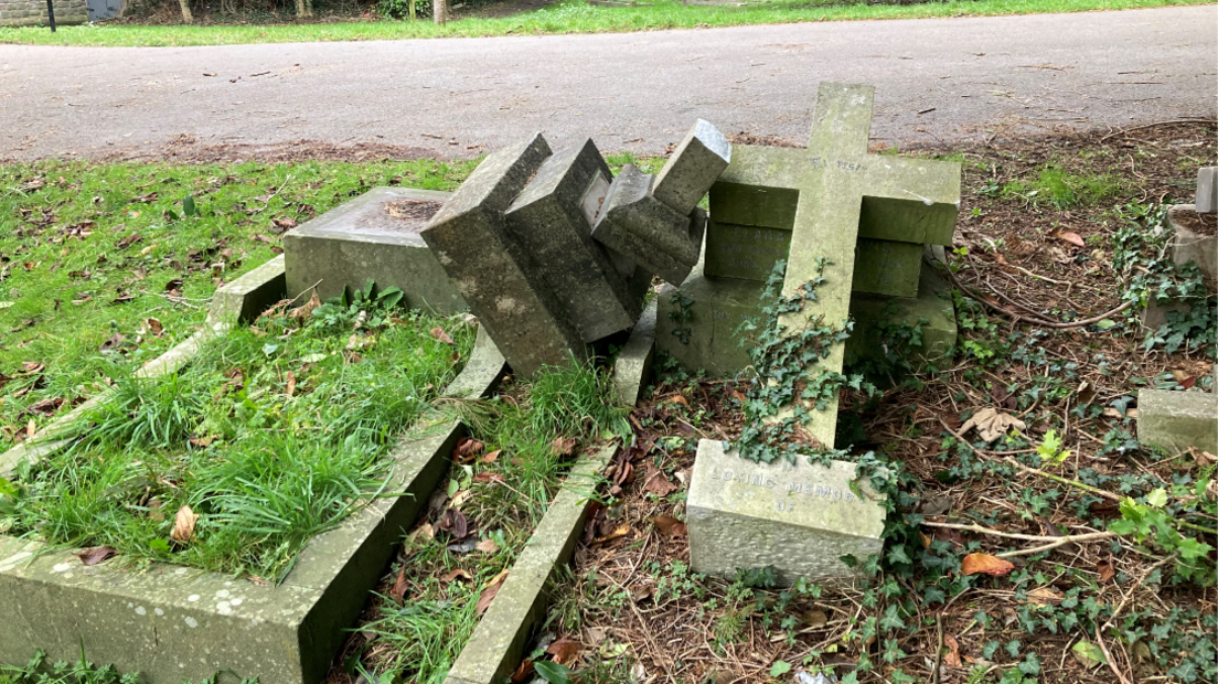 Two graves next to each other with a large tombstone resembling a cross appearing to have been knocked off the left hand grave on to the one on the right