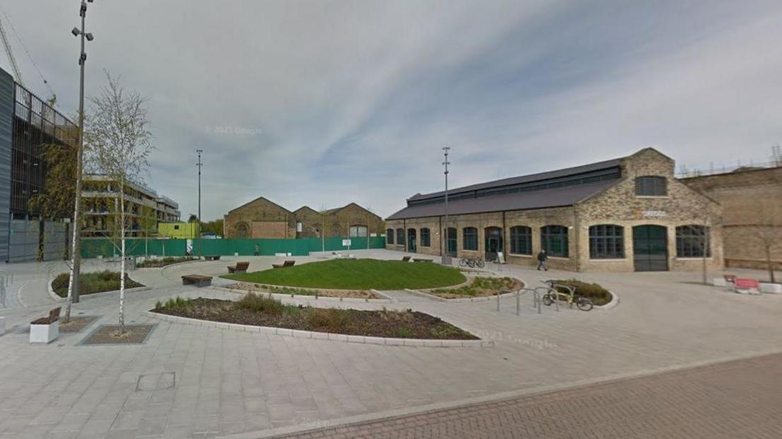 Picture of a green square centre with paving around the outside and flower beds