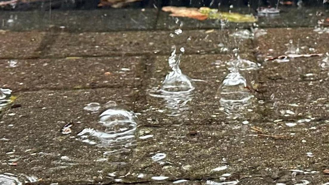 Bubbles are being created on the surface of rainwater on a patio by the drops falling.