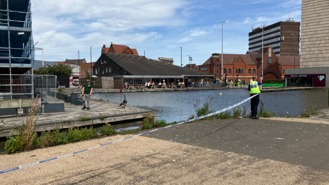 A police officer ties a line of police tape along the edge of the canal in Walsall