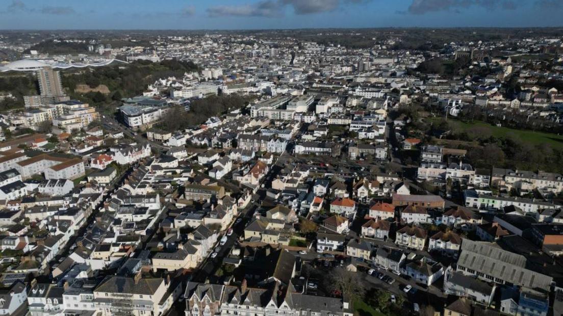 Aerial view of South St Helier with houses, tower blocks and office buildings along with fields, green spaces and trees.