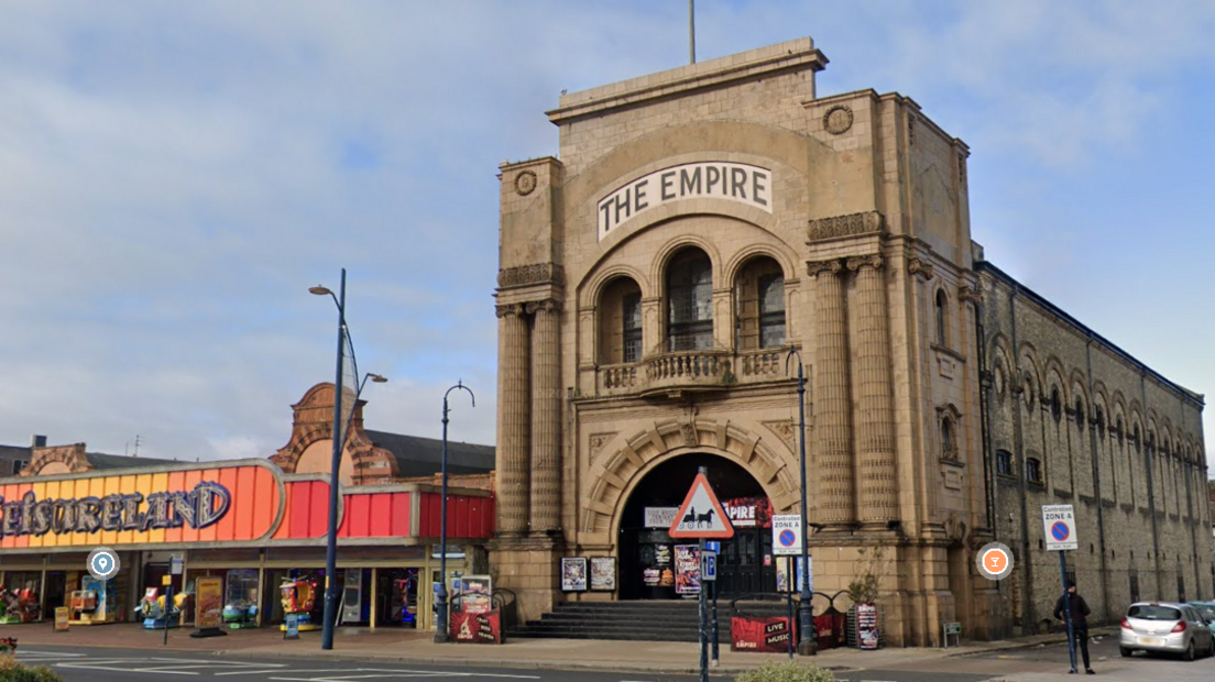 The Empire in Great Yarmouth, a pale brown stone building with pillared facade, next to an amusement arcade on the seafront