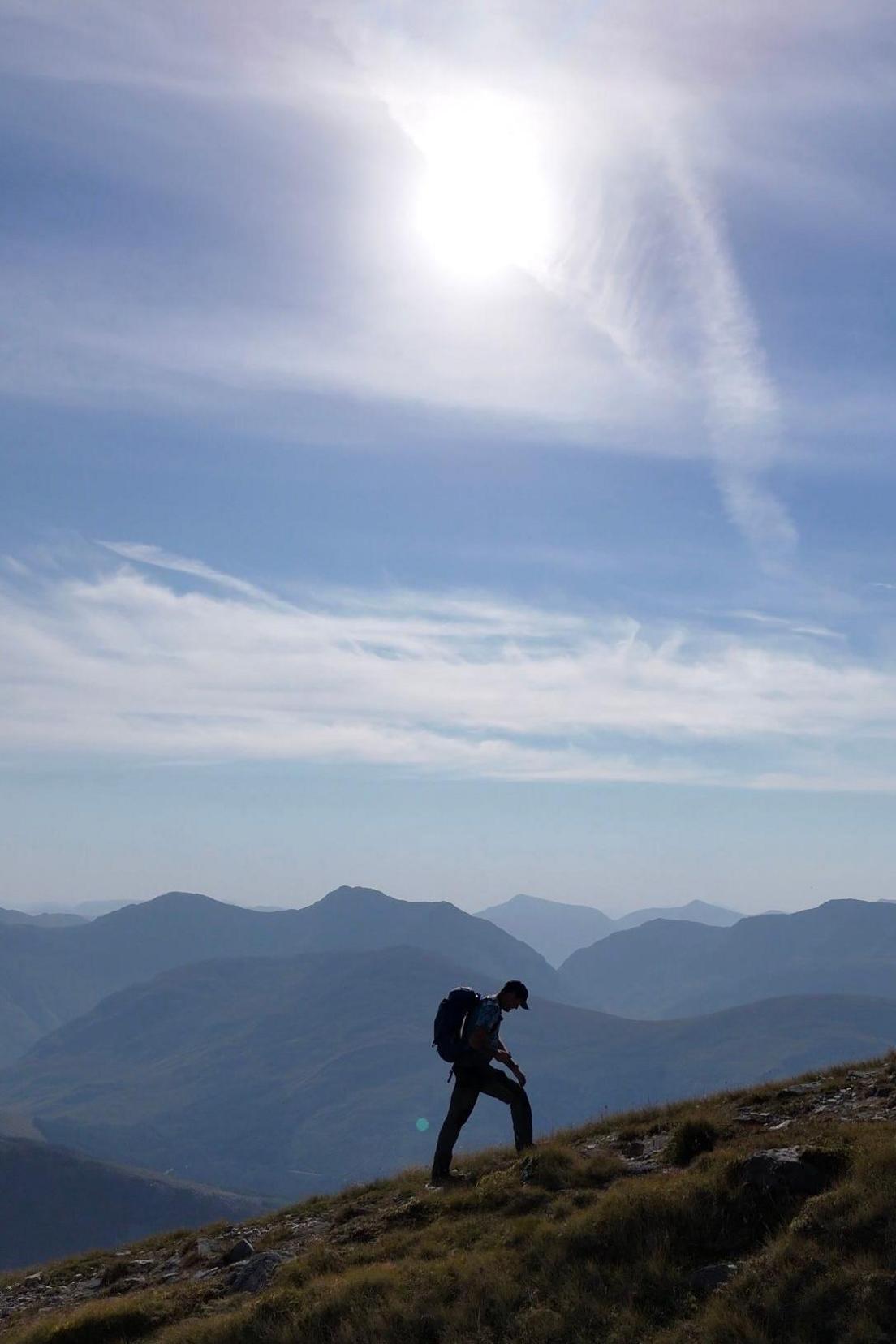 A hillwalker ascending a slope against a backdrop of mountains